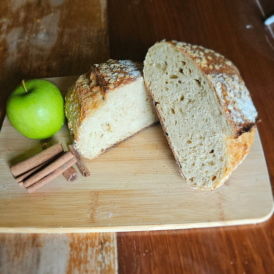 Sliced bread on a wooden cutting board with an apple and cinnamon stick.